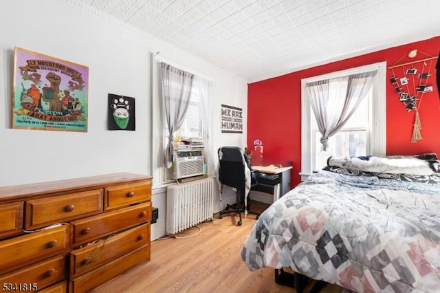 bedroom with light wood-style floors, cooling unit, and radiator