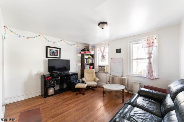 living room with radiator heating unit, cooling unit, wood finished floors, and baseboards