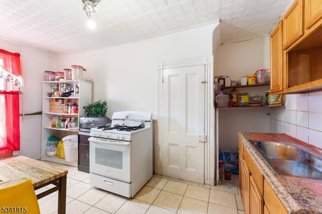 kitchen with light tile patterned flooring, a sink, decorative backsplash, open shelves, and white gas range