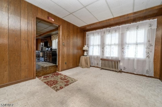 spare room featuring wooden walls, carpet floors, plenty of natural light, and radiator