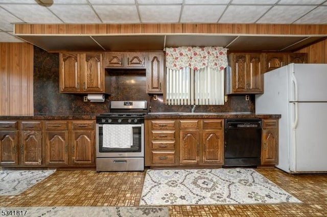 kitchen featuring black dishwasher, freestanding refrigerator, wood walls, and gas range