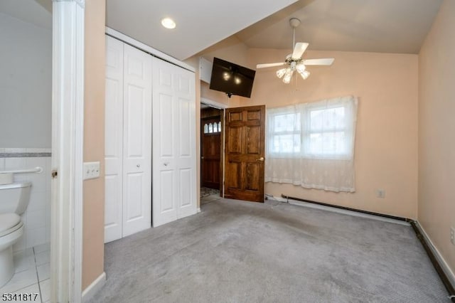 unfurnished bedroom with tile walls, a closet, ensuite bathroom, carpet flooring, and vaulted ceiling