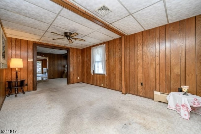 carpeted spare room featuring visible vents, ceiling fan, a paneled ceiling, wood walls, and a baseboard heating unit