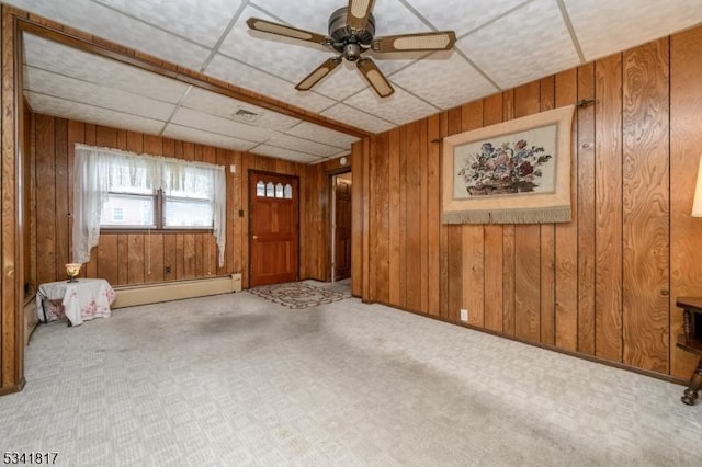 spare room with a paneled ceiling, visible vents, a baseboard heating unit, a ceiling fan, and wood walls