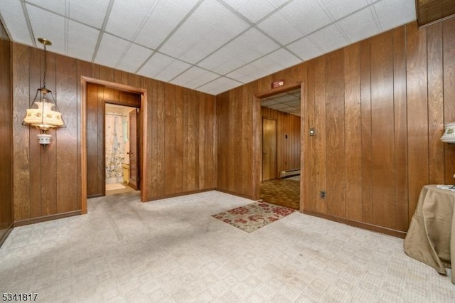 unfurnished room featuring light carpet, a baseboard heating unit, wood walls, and baseboards