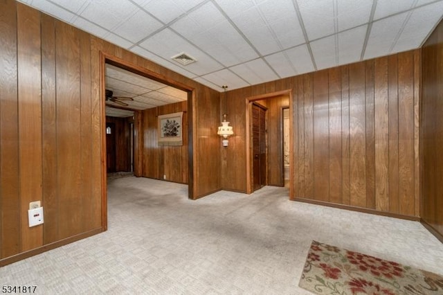 carpeted spare room with a paneled ceiling, a ceiling fan, visible vents, and wooden walls