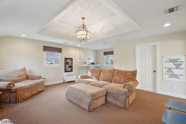 living area with carpet floors, a tray ceiling, plenty of natural light, and visible vents