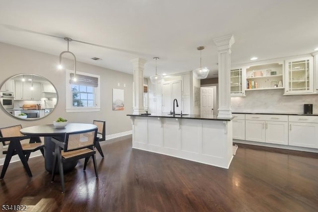 kitchen featuring open shelves, stainless steel appliances, dark countertops, tasteful backsplash, and ornate columns