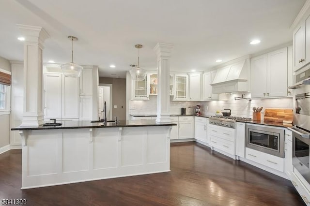 kitchen featuring stainless steel appliances, a sink, dark countertops, decorative columns, and custom range hood