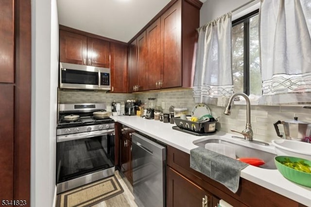 kitchen with a sink, stainless steel appliances, reddish brown cabinets, light countertops, and decorative backsplash