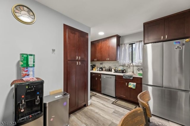 kitchen with backsplash, light countertops, appliances with stainless steel finishes, light wood-style floors, and a sink