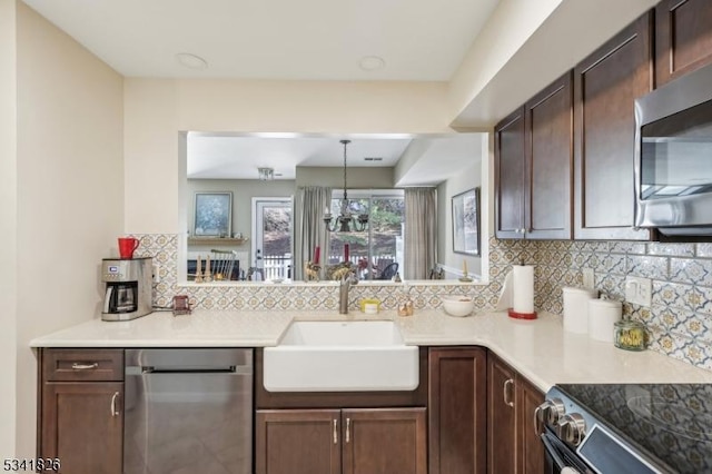 kitchen with a sink, light countertops, appliances with stainless steel finishes, backsplash, and decorative light fixtures