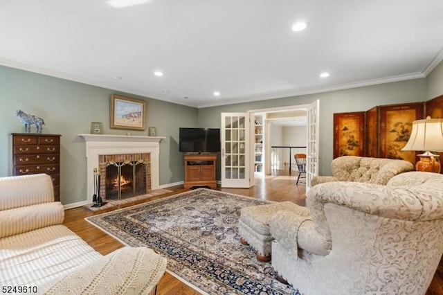 living room with wood finished floors, crown molding, french doors, a brick fireplace, and recessed lighting