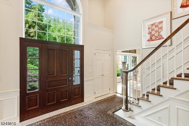 entryway featuring wainscoting, a decorative wall, and a towering ceiling