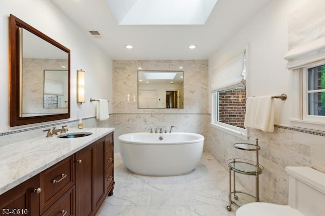 bathroom featuring toilet, a skylight, tile walls, marble finish floor, and a soaking tub