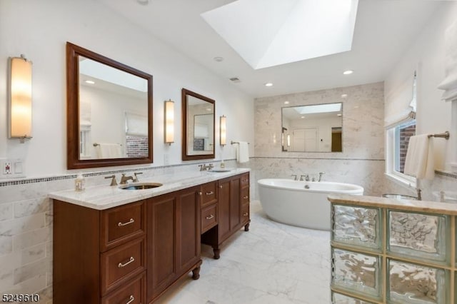 full bath featuring a skylight, marble finish floor, tile walls, a freestanding bath, and a sink