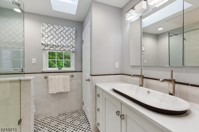 bathroom with a skylight, tiled shower, wainscoting, vanity, and tile walls