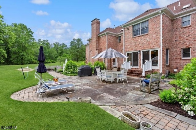 back of house with a patio area, a chimney, a lawn, and brick siding