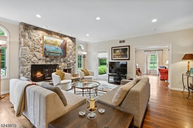 living area featuring ornamental molding, visible vents, a fireplace, and wood finished floors