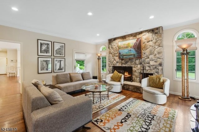 living area featuring ornamental molding, a stone fireplace, wood finished floors, and a wealth of natural light