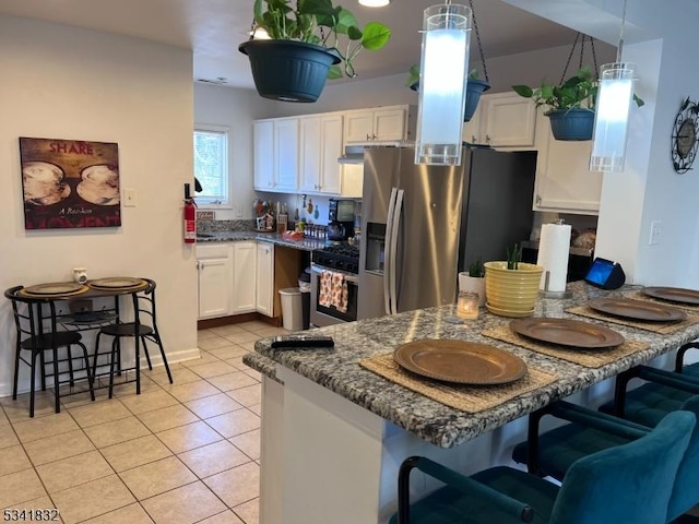 kitchen with light tile patterned floors, white cabinetry, appliances with stainless steel finishes, and a breakfast bar