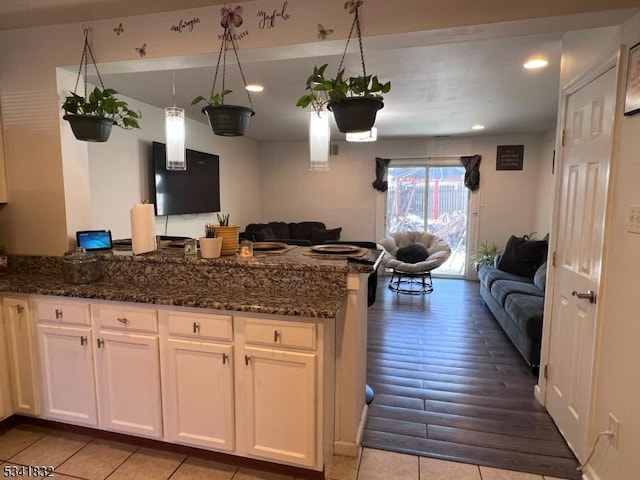 kitchen featuring dark stone counters, open floor plan, white cabinetry, and a peninsula