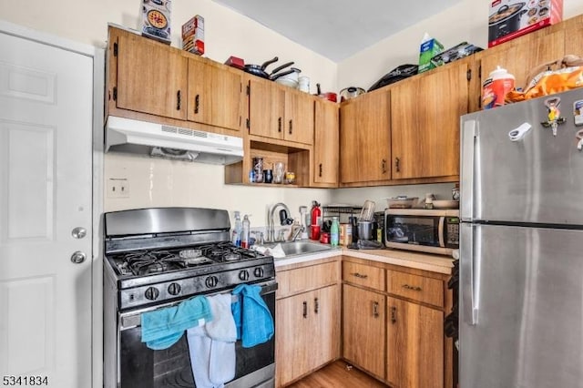 kitchen featuring under cabinet range hood, appliances with stainless steel finishes, light countertops, and a sink