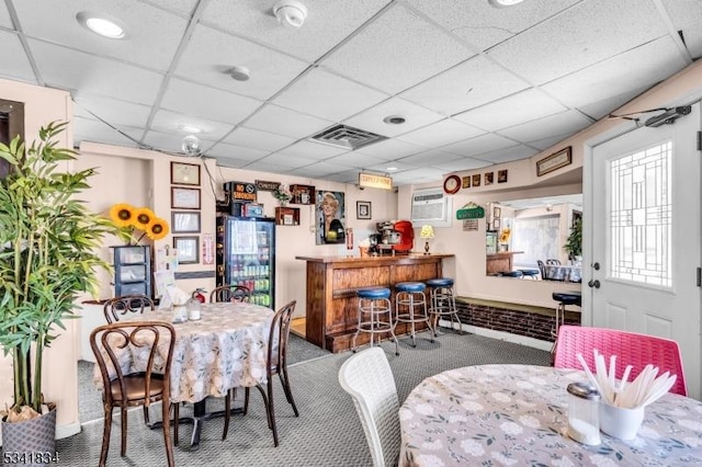 carpeted dining room with a bar, a paneled ceiling, a wall unit AC, and visible vents