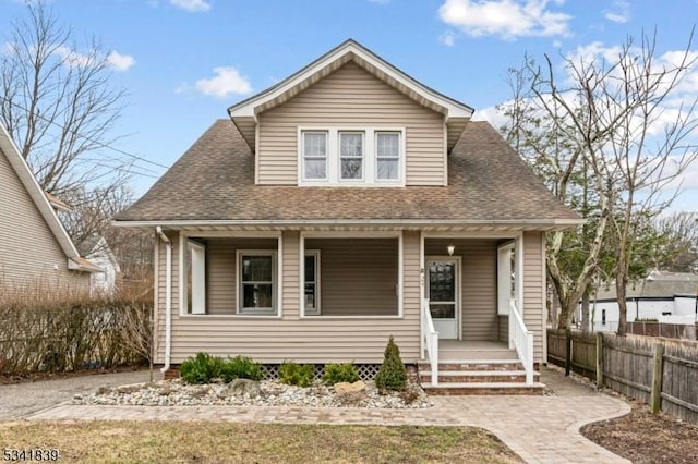 bungalow-style home with covered porch, a shingled roof, and fence