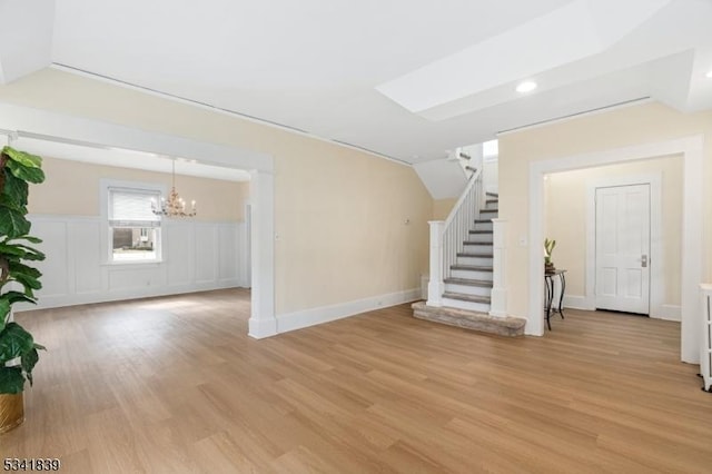 unfurnished living room with vaulted ceiling, stairway, a notable chandelier, and light wood-type flooring