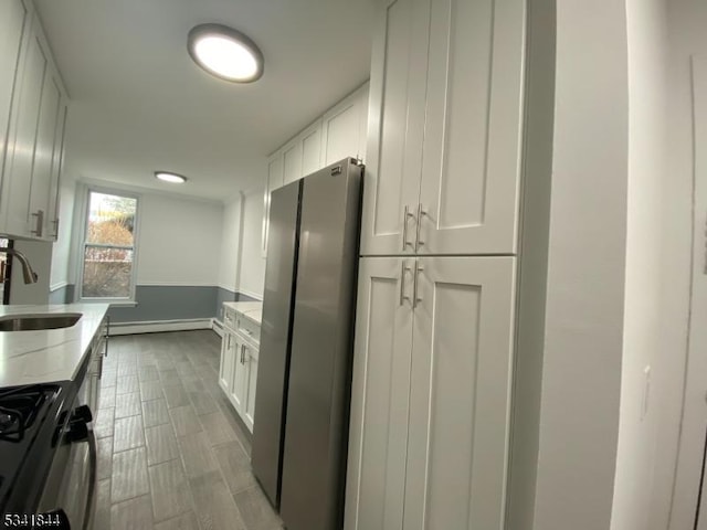 kitchen featuring a baseboard heating unit, a sink, freestanding refrigerator, light stone countertops, and black gas range oven