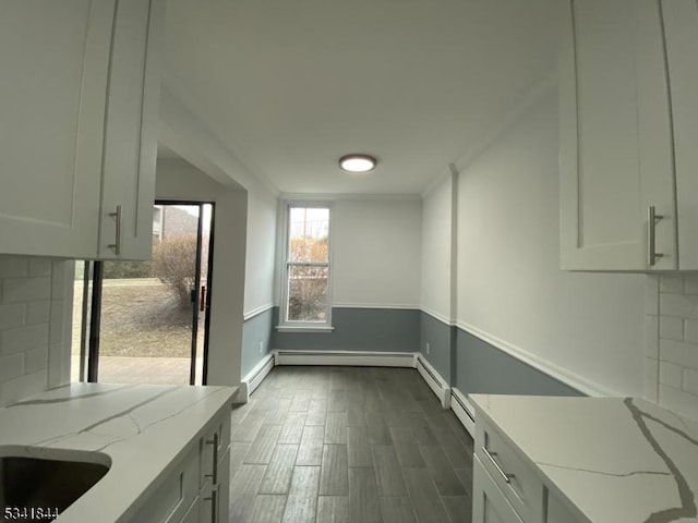 interior space featuring tasteful backsplash, dark wood-type flooring, ornamental molding, light stone countertops, and baseboards