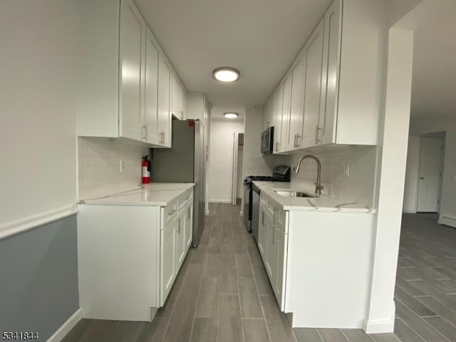 kitchen featuring appliances with stainless steel finishes, wood tiled floor, white cabinets, and a sink