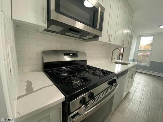 kitchen featuring a baseboard radiator, backsplash, light stone countertops, stainless steel appliances, and a sink