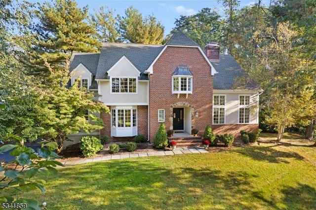 view of front of house featuring brick siding, a chimney, and a front lawn