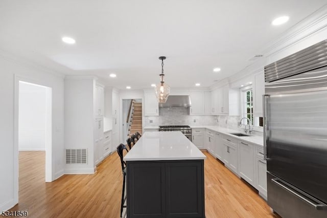 kitchen featuring high end appliances, visible vents, a kitchen island, a sink, and under cabinet range hood