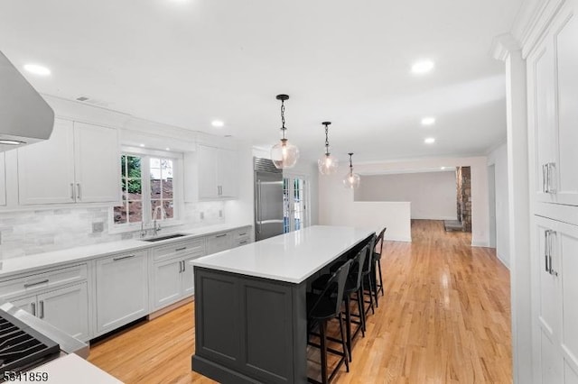 kitchen featuring built in refrigerator, a sink, a kitchen bar, white cabinetry, and backsplash