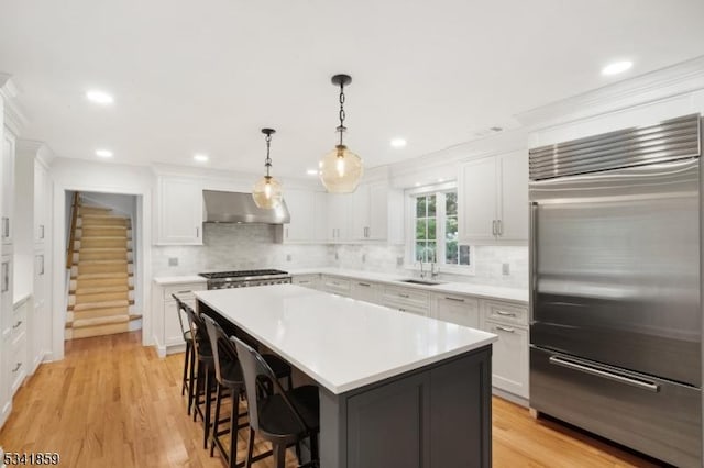 kitchen featuring a breakfast bar area, built in refrigerator, ventilation hood, light countertops, and a sink