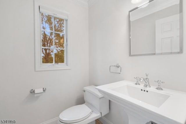 half bath featuring crown molding, baseboards, a sink, and toilet