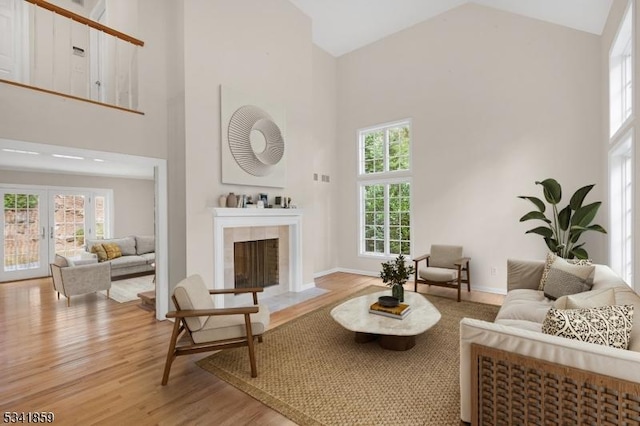 living area with a tiled fireplace, high vaulted ceiling, light wood finished floors, and plenty of natural light