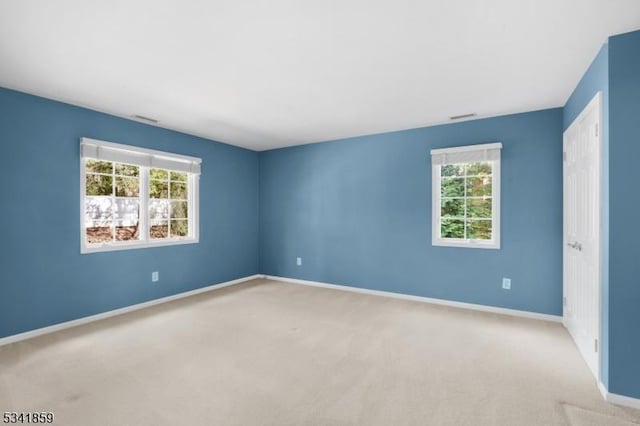 carpeted spare room with a healthy amount of sunlight, visible vents, and baseboards