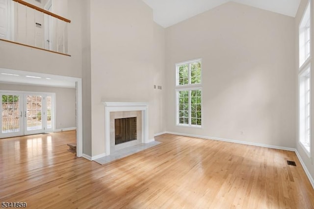 unfurnished living room featuring visible vents, light wood-style flooring, a healthy amount of sunlight, a fireplace, and high vaulted ceiling