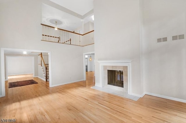 unfurnished living room with a fireplace, visible vents, wood finished floors, baseboards, and stairs