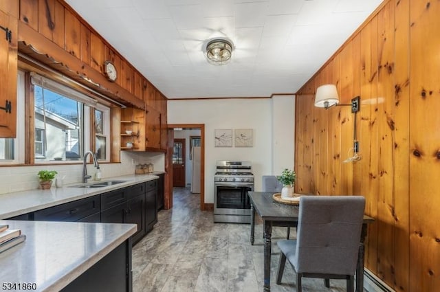 kitchen with light countertops, backsplash, stainless steel range with gas stovetop, a sink, and wood walls