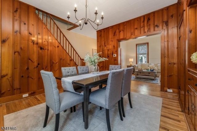 dining space with a chandelier, stairway, wood walls, and light wood-style flooring