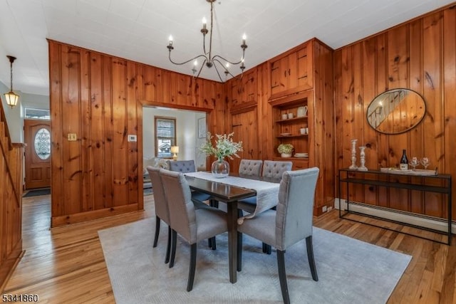 dining area featuring light wood finished floors, wooden walls, baseboard heating, and an inviting chandelier