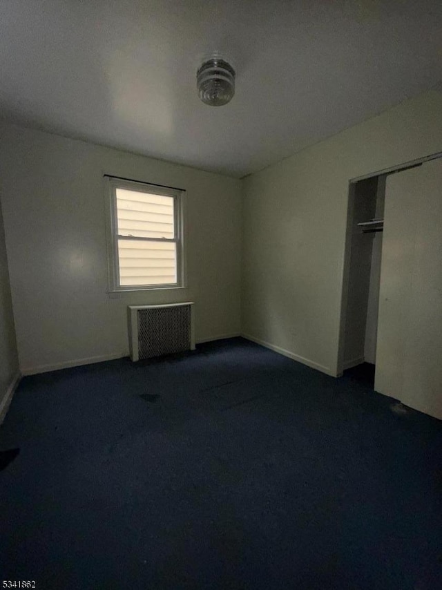 unfurnished bedroom with a closet, dark carpet, and radiator