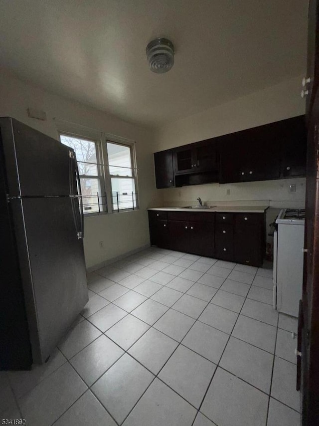 kitchen featuring white gas range, light countertops, freestanding refrigerator, light tile patterned flooring, and a sink