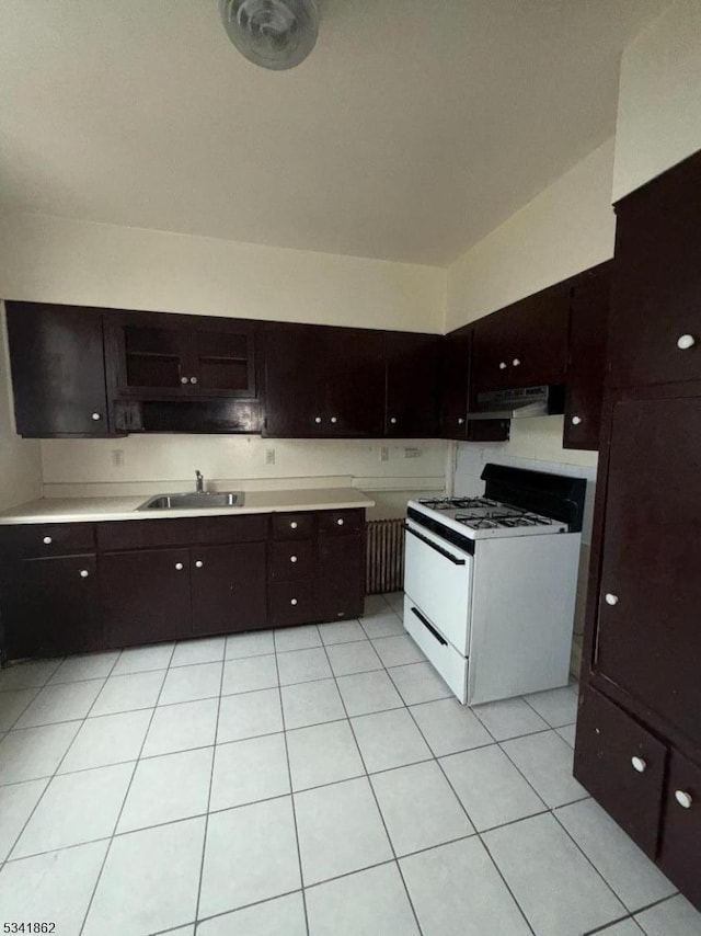 kitchen featuring light tile patterned floors, white range with gas stovetop, light countertops, under cabinet range hood, and a sink