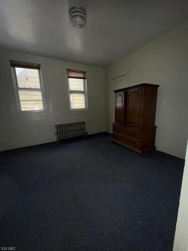 spare room featuring radiator and dark colored carpet